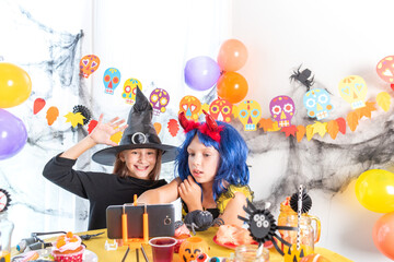 Dressed in spooky halloween costumes girls headwear having video chat on laptop with friends in decorated home.