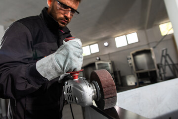 Industrial worker with angle grinder working and polishing stainless steel structure at workshop.