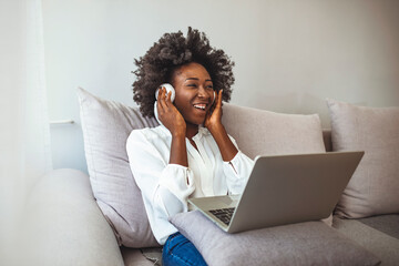 Portrait of a young woman relaxing on couch and listening to music using laptop and headphones. A young female student sitting on the sofa, using headphones when studying