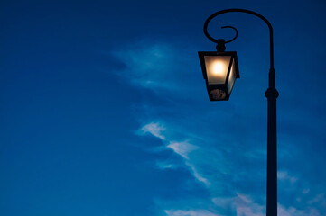 Fototapeta na wymiar Classic electric lamp lighting and shining against dark blue sky at dusk, copy space.