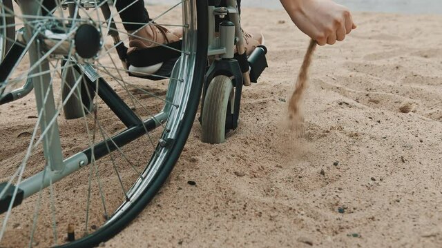 Disabled person in the wheelchair playing with the sand on the beach, close up. High quality 4k footage
