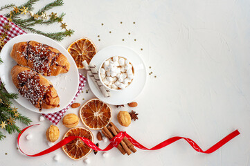Fototapeta na wymiar Christmas breakfast. Christmas morning. A cup of cocoa with marshmallows and croissants on a light concrete background with a branch of decorated Christmas tree. Place for text. View from above.
