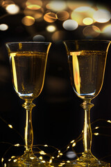 Christmas background concept. Two glasses with champagne and garland lights on a black background.
