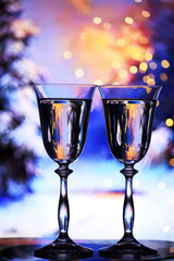 Two glasses of champagne against the backdrop of a winter fabulous landscape. Glittering lights and the reflection of garlands in the glass. Christmas background concept.
