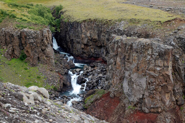 Water stream falls from a red rock. Location: Hengifoss hiking trail, East iceland.