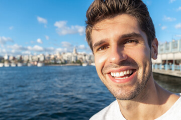 Portrait of a young handsome tourist man with a big smile taking a picture with Galata tower in...