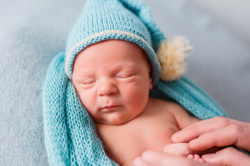 Adorable newborn baby wrapped in a beautiful fabric, woolen scarf and with a small hat on his head