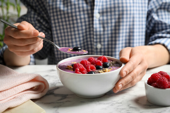 Woman eating tasty acai smoothie with fruits at white marble table, closeup