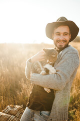 Portrait of stylish young hipster with a cat. Relaxing moment. Hister men is hugging a cat at sunset. The concept of youth, love and lifestyle.
