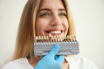 Doctor matching patient's teeth color with palette on white background, closeup. Cosmetic dentistry