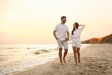 Happy young couple walking together on beach at sunset