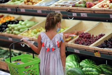 A girl in a medical mask in a supermarket buys vegetables and fruits.