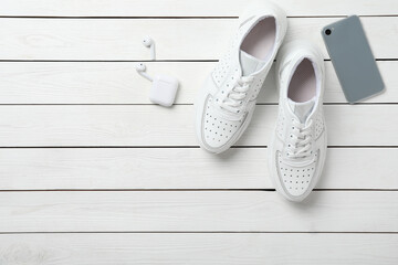 Pair of stylish shoes, modern smartphone and wireless earphones on white wooden table, flat lay. Space for text