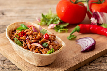 Mexican barquita taco with beef, chilli, tomato, onion and spices on wooden table