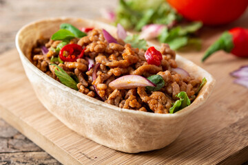 Mexican barquita taco with beef, chilli, tomato, onion and spices on wooden table