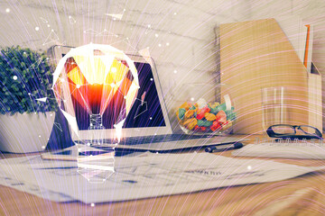 Computer on desktop in office with bulb icon hologram. Double exposure. Concept of idea.