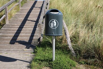 green trash can is standing at a dune at the beach
