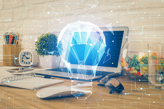 Computer on desktop in office with bulb icon hologram. Double exposure. Concept of idea.