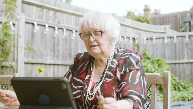 Elderly Woman talking naturally on Skype on a tablet device in the garden day