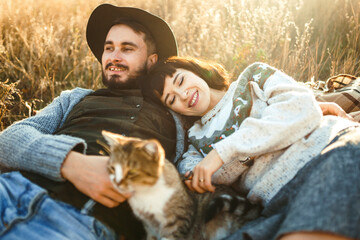 Stylish and loving hipster couple with cat on a sunny day in the park.  Couple wearing beautiful hats and sweaters. The concept of youth, love, autumn and lifestyle.