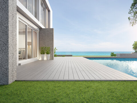 Empty Outdoor Wooden Floor Terrace Near Swimming Pool And Green Grass Garden In Modern Beach House Or Luxury Villa. Building Exterior 3d Rendering With Sea View.