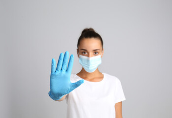 Woman in protective mask showing stop gesture on grey background. Prevent spreading of COVID‑19