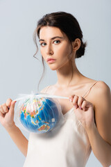young brunette woman holding plastic bag with globe and looking at camera isolated on white, ecology concept