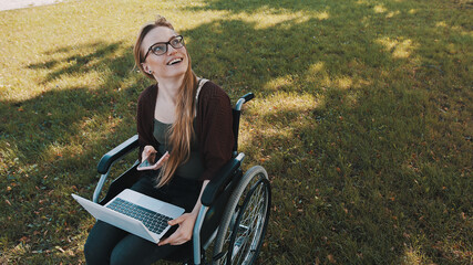 happy young woman in wheelchair with laptop and smartphone looking up in the sky. High quality photo