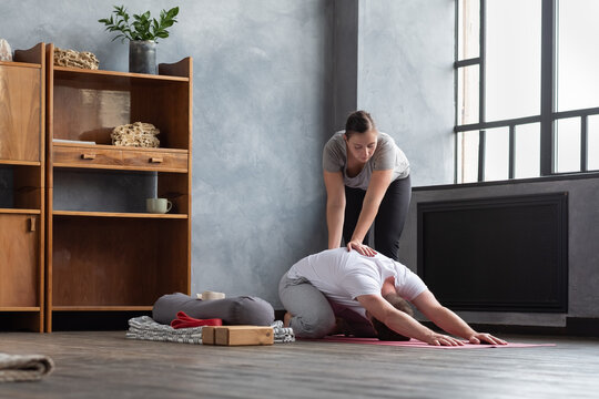 Caucasian female yoga teacher helping to stretch muscles her student doing balasana pose.