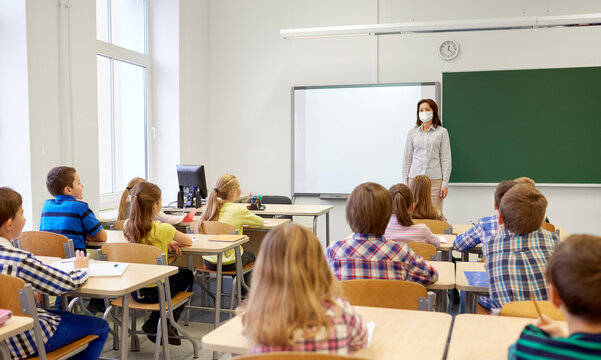 Education, School And Pandemic Concept - Group Of Kids Or Students With Teacher Wearing Face Protective Medical Mask For Protection From Virus Disease In Classroom