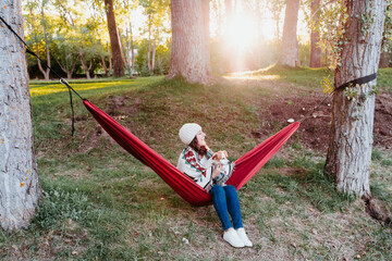 young woman relaxing with her dog in orange hammock. Covering with blanket. Camping outdoors. autumn season at sunset