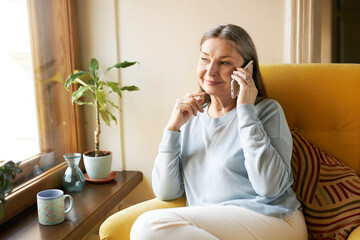 Age, leisure, technology and electronic gadgets. Cheerful casually dressed senior woman with gray...