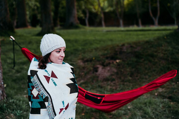 young woman covering with blanket standing next to hammock. autumn season. camping concept