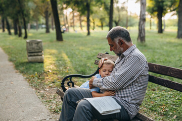 grandfather hugging his grandson while sitting on the bench in the park