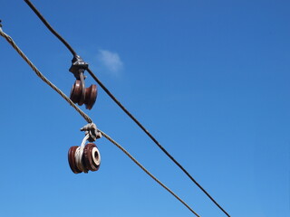 Brown insulators are damaged. An old electric fuse is hanging on a potentially dangerous low voltage line. On the blue sky background with white clouds. Selective focus