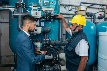 industry worker and his supervisor talking by the chemical water treatment equipment