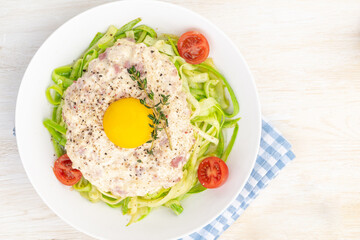 Carbonara sauce. Fried ham in heavy cream and with raw egg yolk and cherry tomatoes. Carbonara pasta made with fresh zucchini noodles.