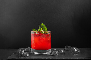 Berry lemonade in a glass with red berries and ice on a black background. Copy space