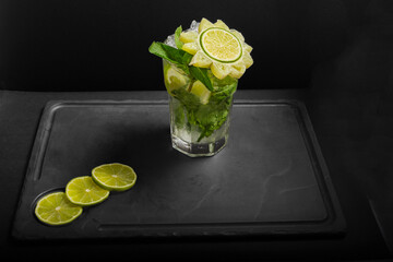 The top view of glass with cold natural oranges lemonade with ice, lime, mint are on a black background. Copy space.