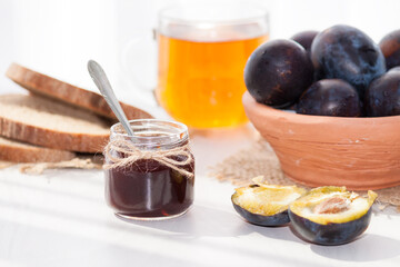 Sweet homemade plum jam and fruits on a white table in a sunny day.