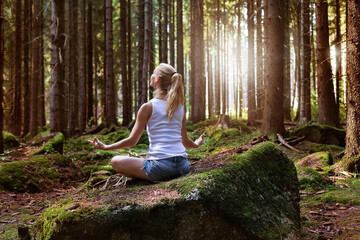 Beautiful woman with long blond hair meditating in forest enjoys the silence of nature.  Self-isolation in the open air	