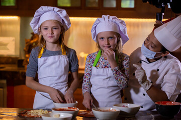 Kid cooking class. Two little girls and teacher chef in kitchen during master class learning how to make pizza