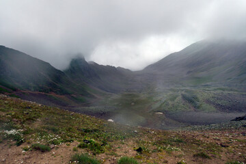 Mountain range in the clouds. Mountain pass in the fog. View from the Pastushiy pass (3244 meters above sea level) to the mountain valley, Caucasus.