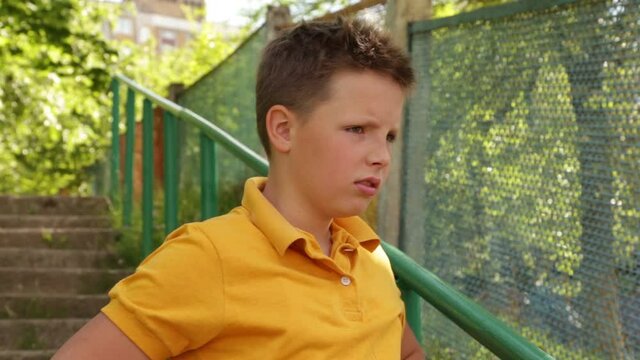 A teenager in a yellow T-shirt cries and is offended. The boy stands on the stairs angry and waving his hand. Boy is in a state of resentment and depression.