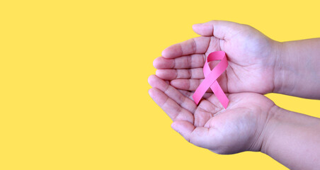 Woman holding pink ribbon on yellow background in studio ,Cancer awareness concept.