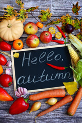 Vertical layout of autumn harvest of vegetables and fruits on a wooden background with text Hello Autumn. Vegan organic food. Top view