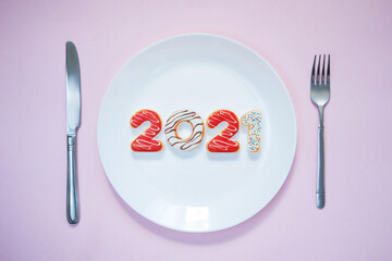 Plate with numbers 2021, knife and fork on pink background. Restaurant and food theme. Christmas. New Year . New Year's menu
