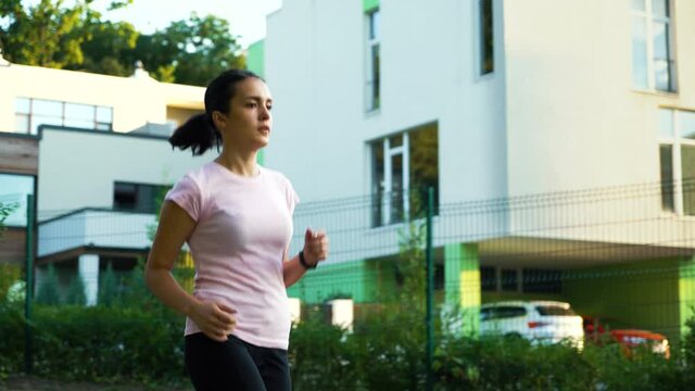 Young woman in sportswear jogging in city, buildings on background. Fit female doing cardio training outside. Concept of sport