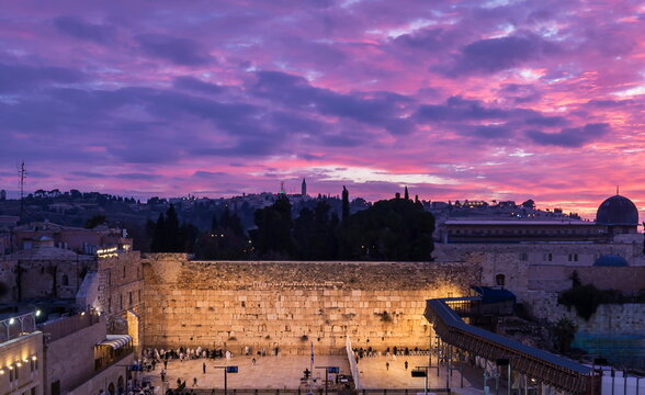 Jewish people praying Shacharit at the Western/Wailing Wall (Kotel) - holiest place in Judaism, and the Temple Mount with beautiful purple sunrise clouds; Jerusalem Israel