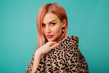 Close up studio portrait of stunning woman with pink hairs in stylish winter fluffy  coat with leopard print on  vivid   turquoise  background.